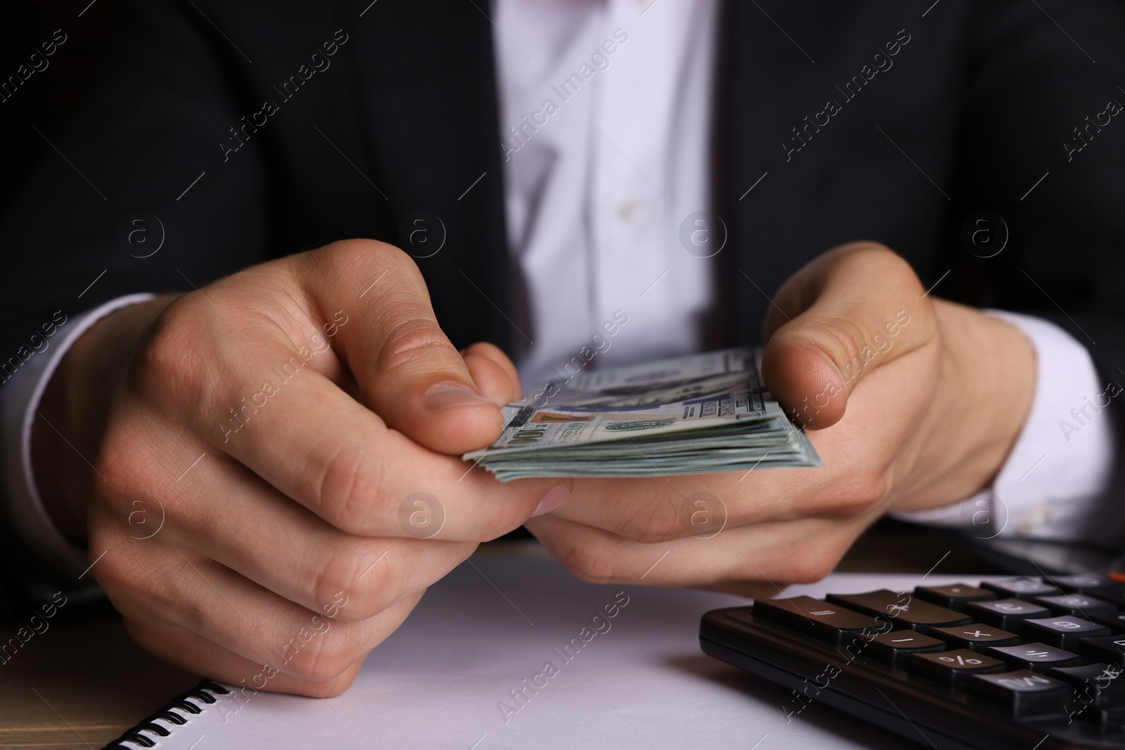 Photo of Money exchange. Man holding dollar banknotes at wooden table, closeup