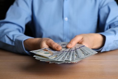 Photo of Money exchange. Woman holding dollar banknotes at wooden table, closeup