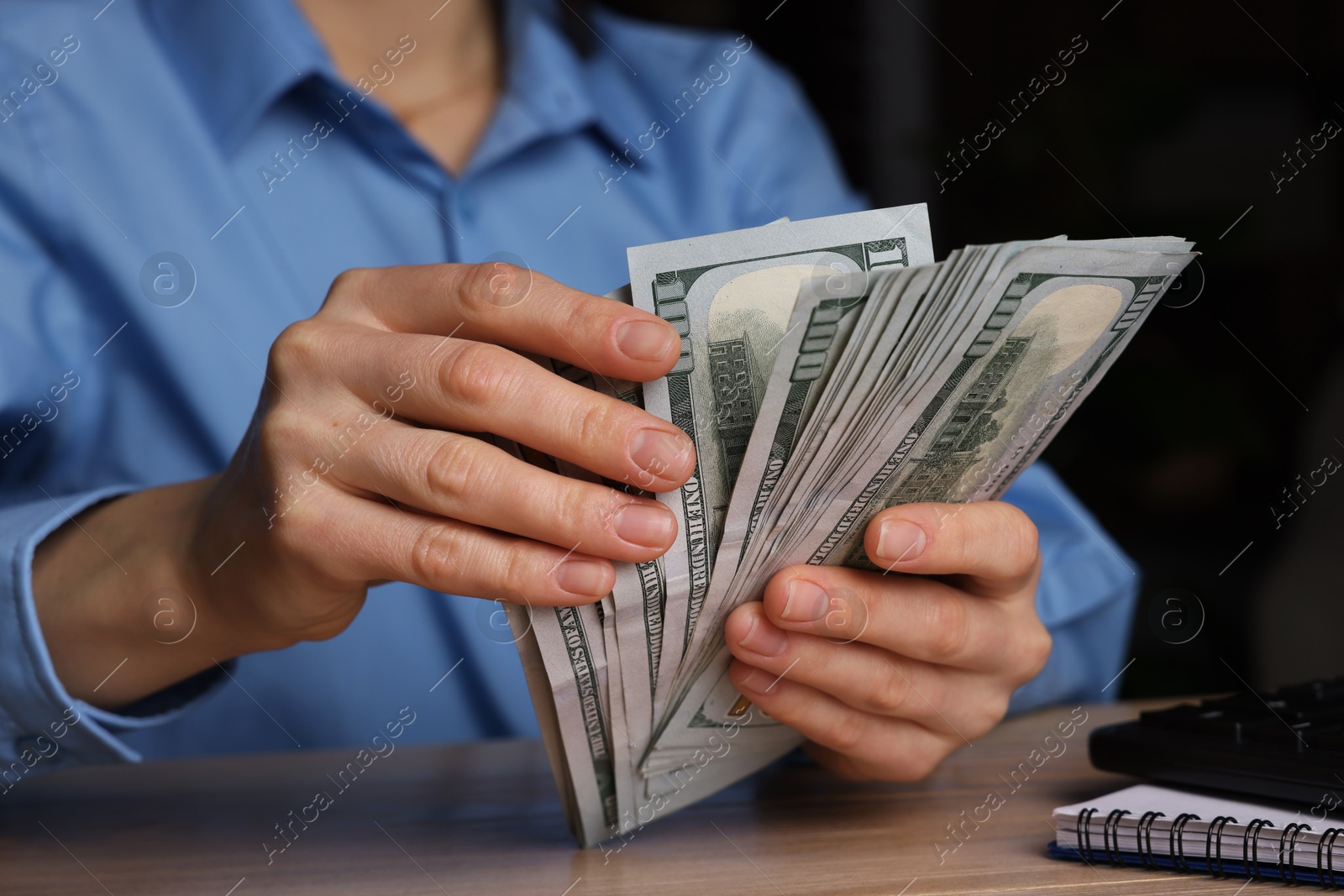 Photo of Money exchange. Woman counting dollar banknotes at wooden table, closeup