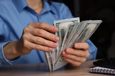 Photo of Money exchange. Woman counting dollar banknotes at wooden table, closeup