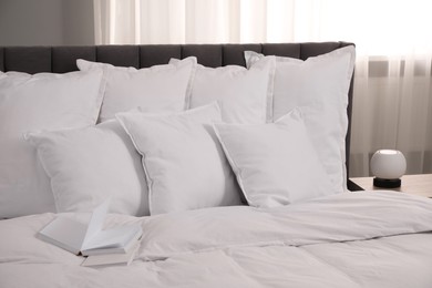 Many soft white pillows and duvet on bed indoors