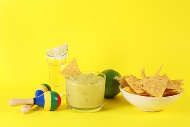 Photo of Delicious guacamole with nachos chips, maracas, tequila and lime on yellow background, space for text