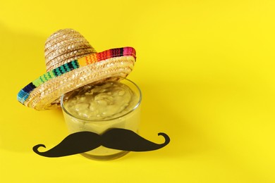 Photo of Delicious guacamole, Mexican sombrero hat and fake mustache on yellow background. Space for text