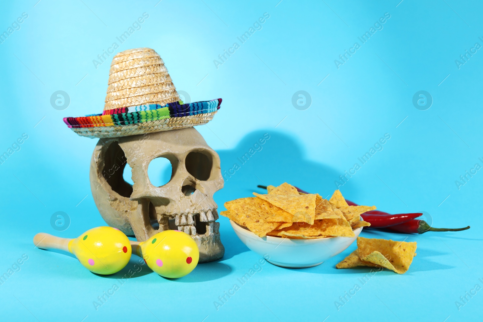 Photo of Human scull with Mexican sombrero hat, maracas and nachos chips on light blue background