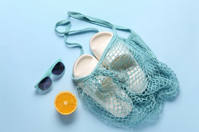 Photo of String bag, sunglasses, orange and slippers on light blue background, top view