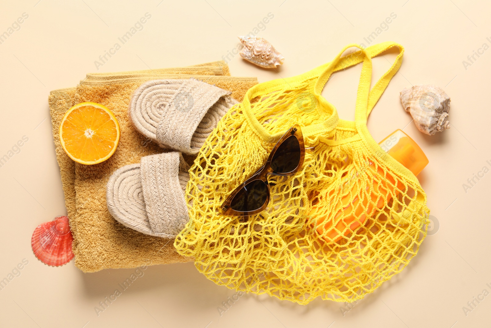 Photo of String bag, different beach accessories and orange on beige background, top view