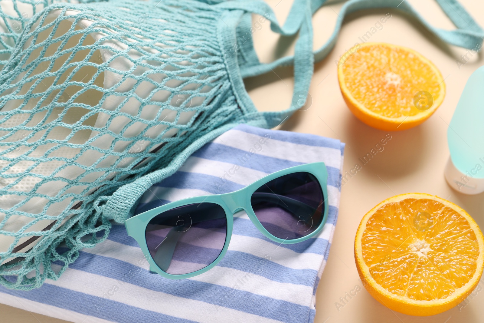 Photo of String bag, different beach accessories and orange on beige background