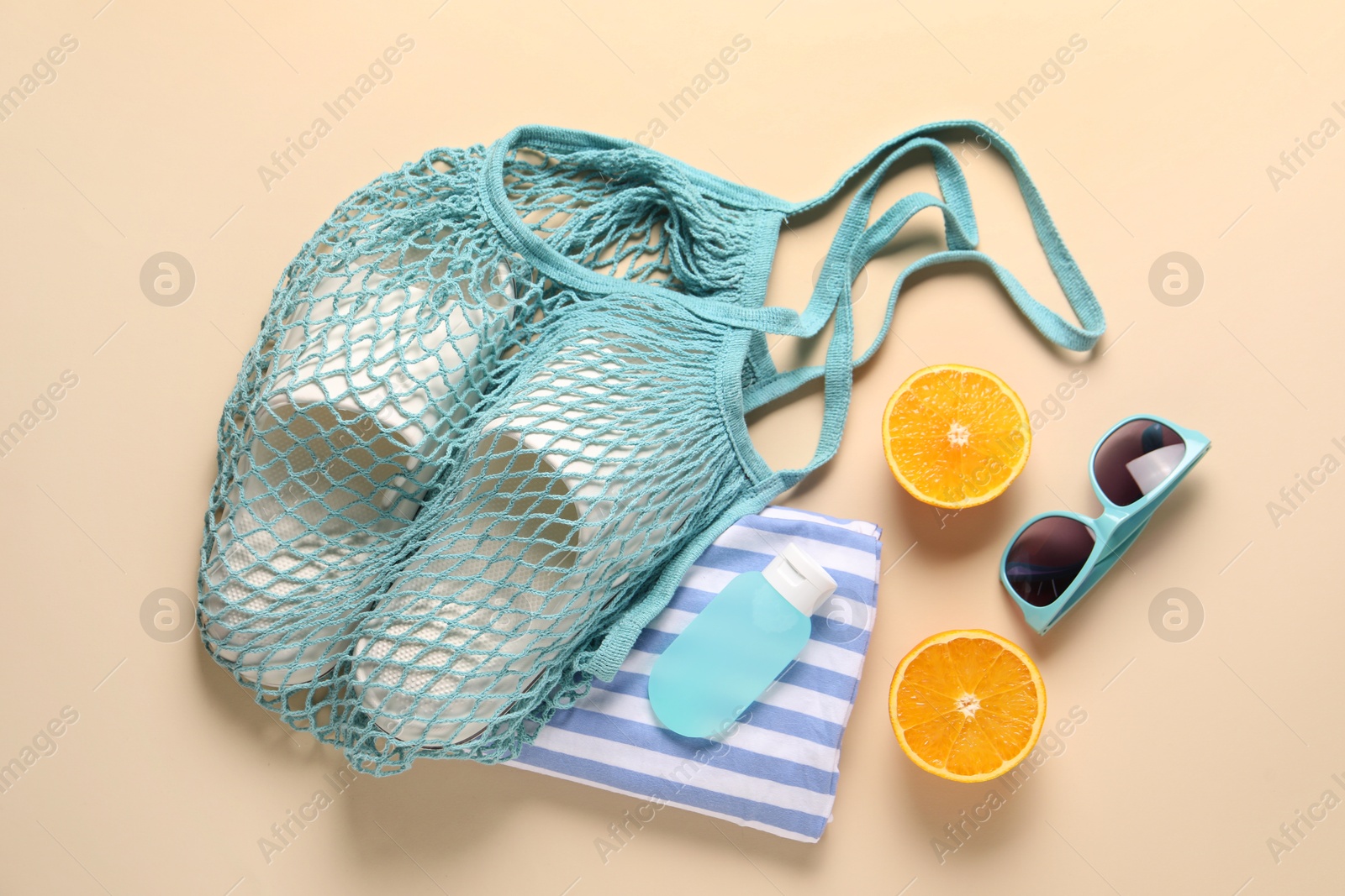 Photo of String bag, different beach accessories and orange on beige background, flat lay