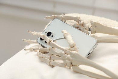 Waiting concept. Human skeleton with smartphone sitting in armchair indoors, closeup