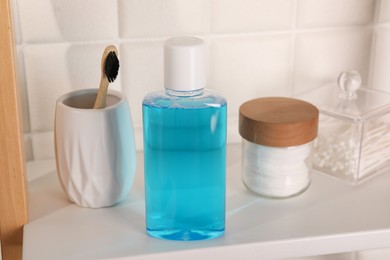 Photo of Bottle of mouthwash, toothbrush, cotton buds and pads on white shelf in bathroom