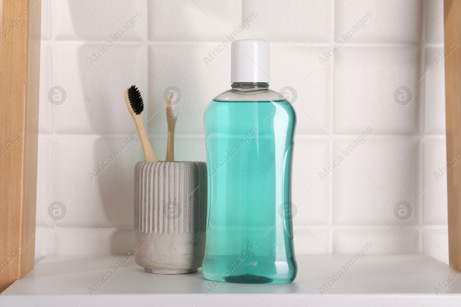 Photo of Bottle of mouthwash and toothbrushes on white shelf in bathroom