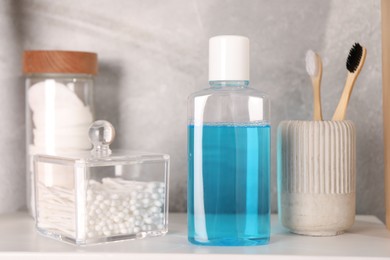 Photo of Bottle of mouthwash, toothbrushes, cotton buds and pads on white shelf in bathroom