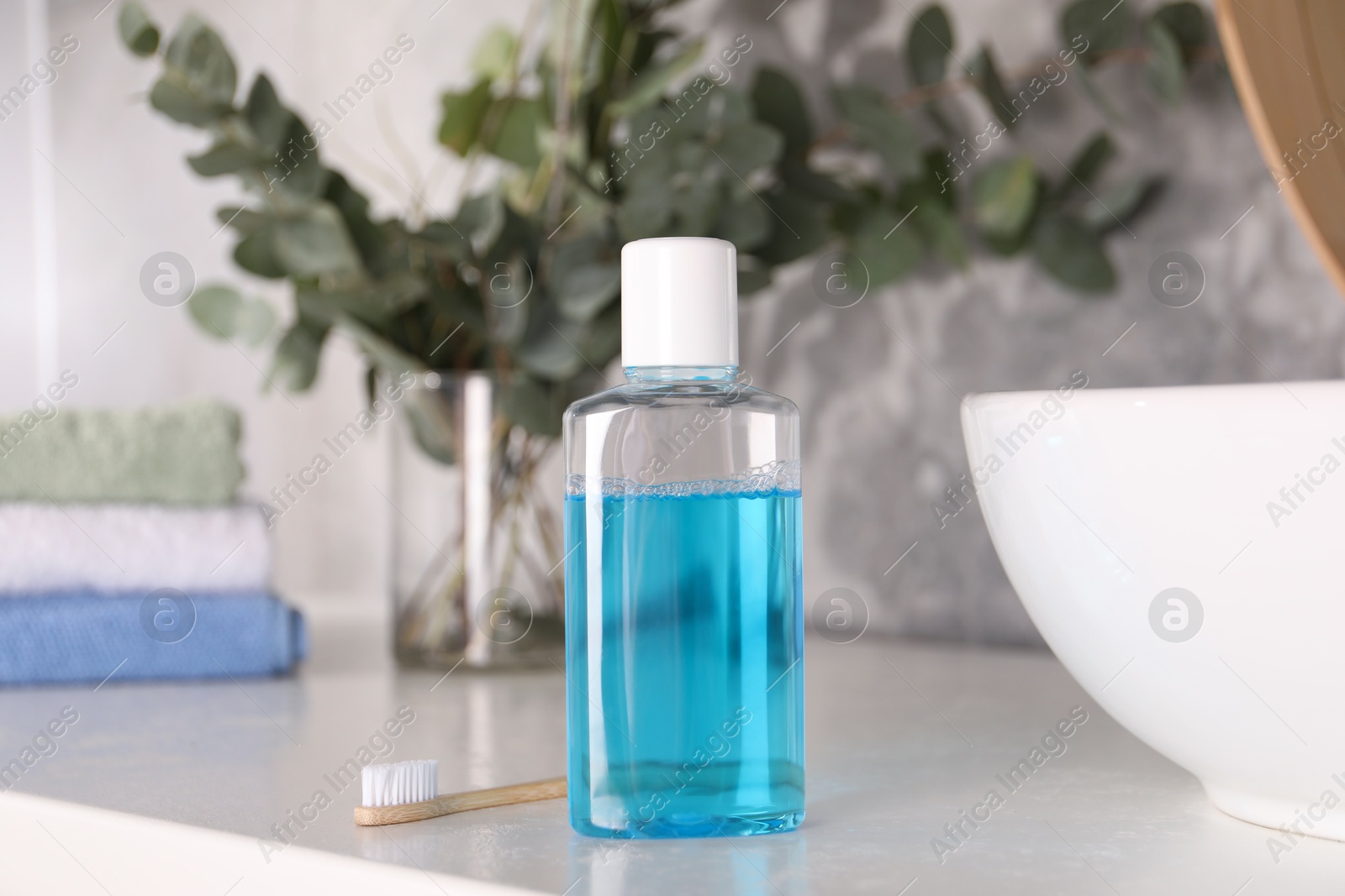 Photo of Bottle of mouthwash and toothbrush on white table in bathroom
