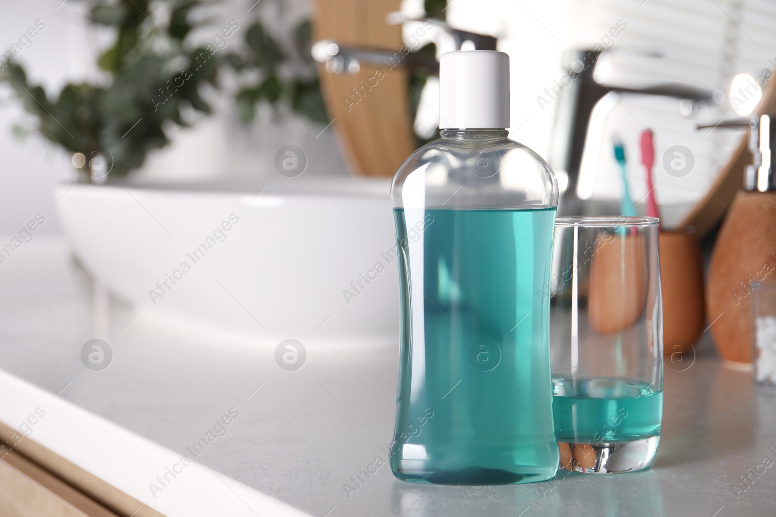 Photo of Bottle and glass of mouthwash on light countertop in bathroom