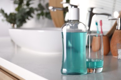 Bottle and glass of mouthwash on light countertop in bathroom