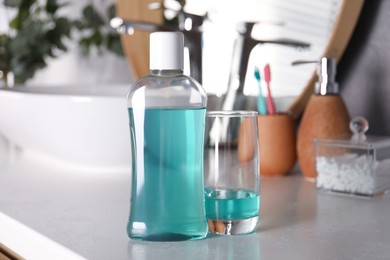 Photo of Bottle and glass of mouthwash on light countertop in bathroom