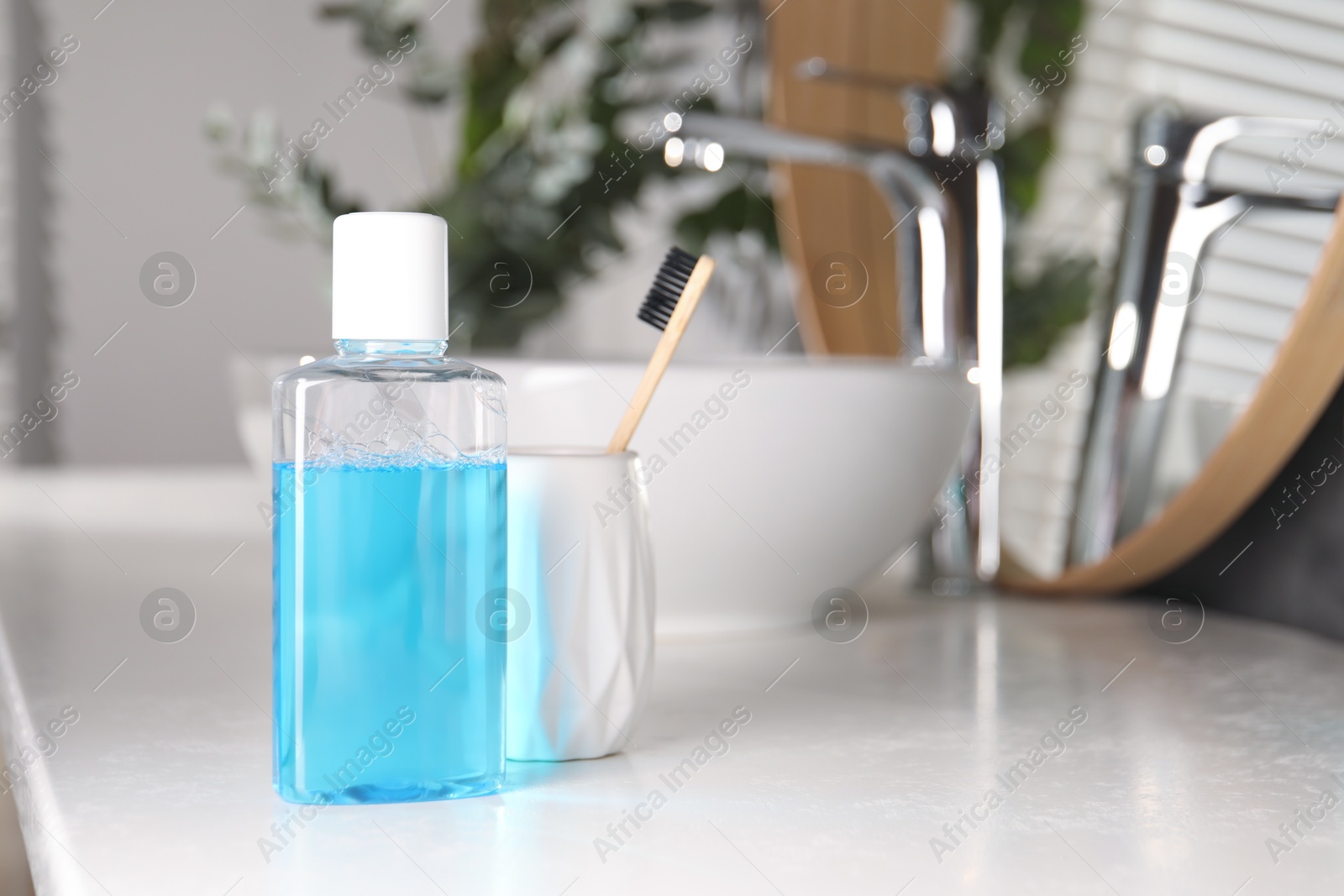 Photo of Bottle of mouthwash and toothbrush on white countertop in bathroom