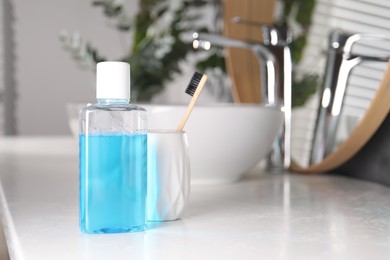 Photo of Bottle of mouthwash and toothbrush on white countertop in bathroom