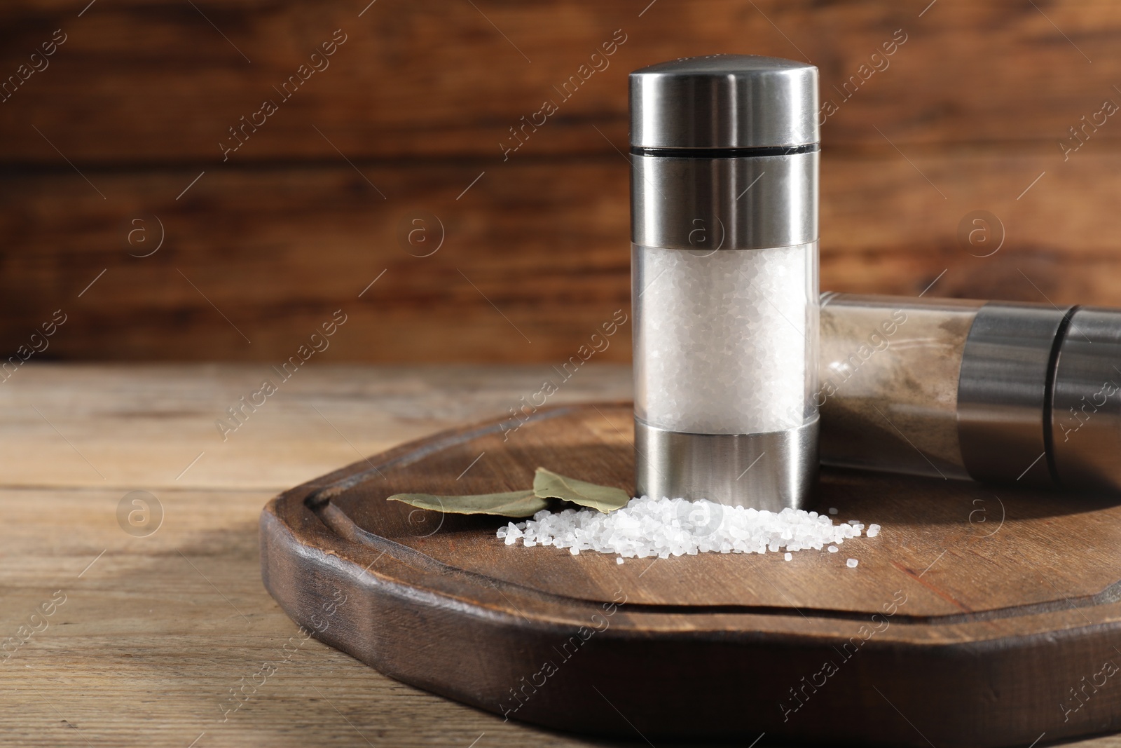 Photo of Salt and pepper shakers with bay leaves on wooden table, space for text