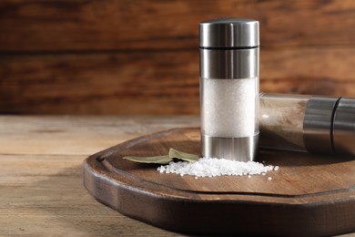 Photo of Salt and pepper shakers with bay leaves on wooden table, space for text