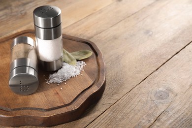 Photo of Salt and pepper shakers with bay leaves on wooden table, space for text