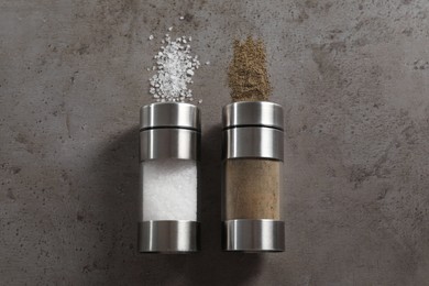 Photo of Salt and pepper shakers on grey textured table, flat lay