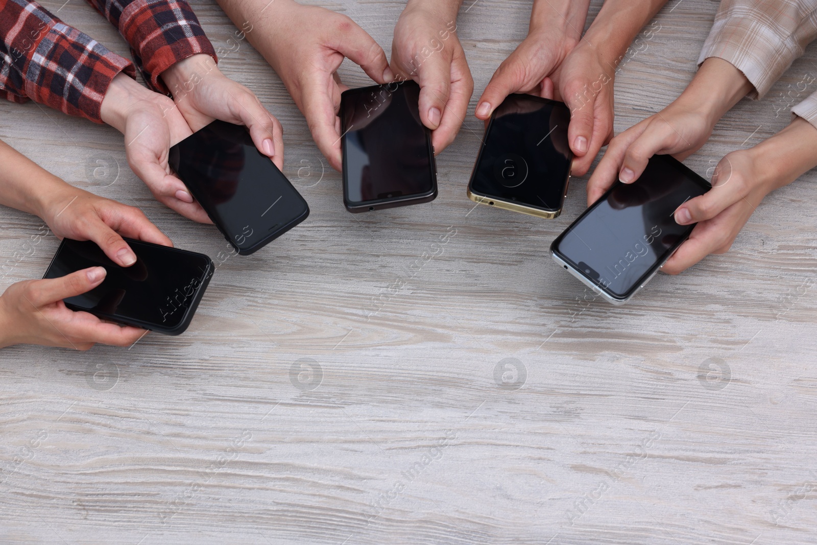 Photo of People holding smartphones with blank screens at wooden table, top view. Mockup for design