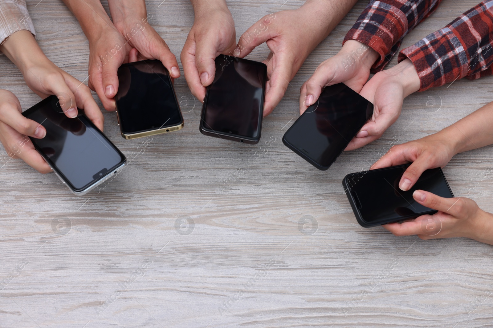 Photo of People holding smartphones with blank screens at wooden table, top view. Mockup for design