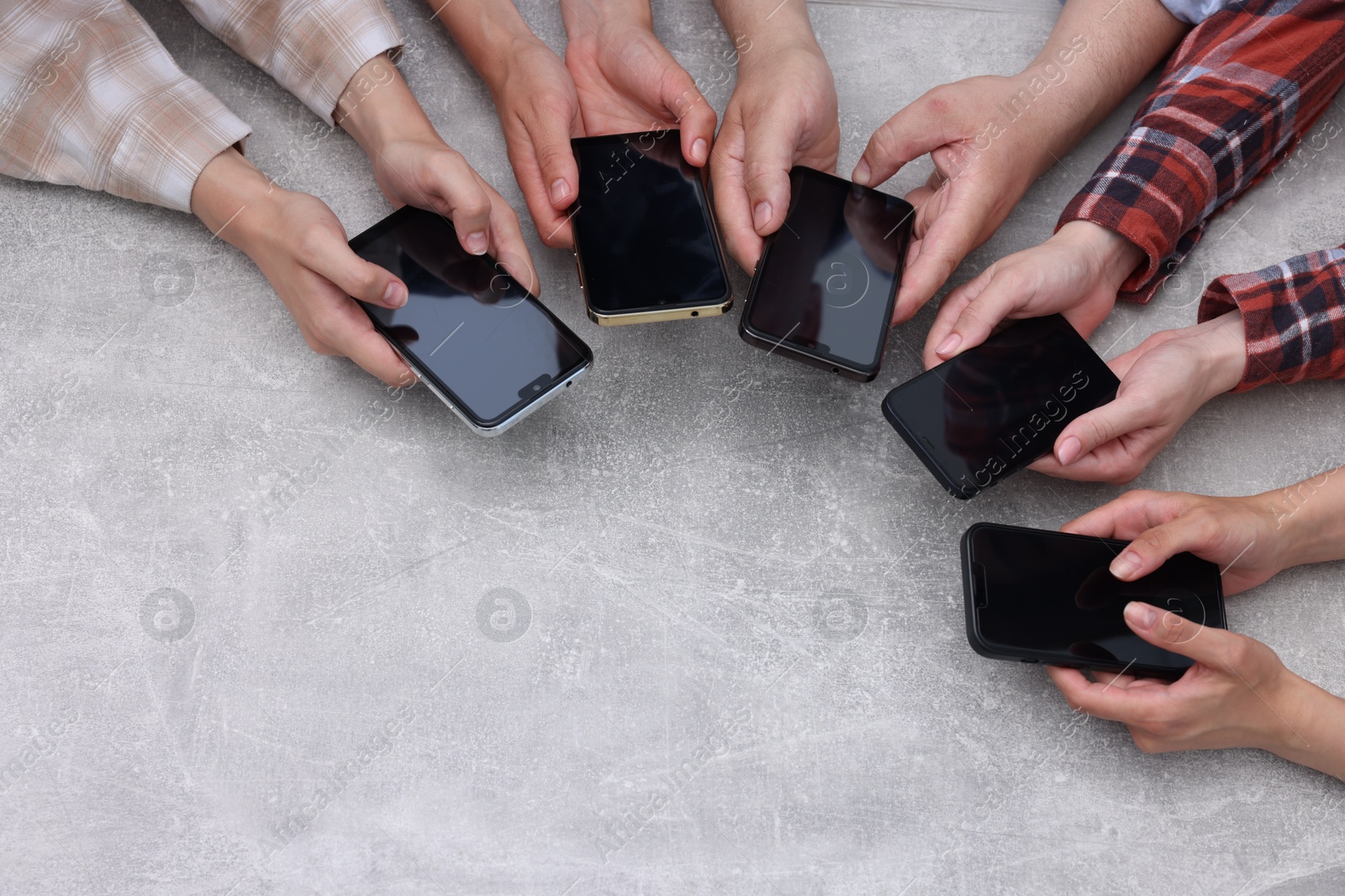 Photo of People holding smartphones with blank screens at grey textured table, top view. Mockup for design