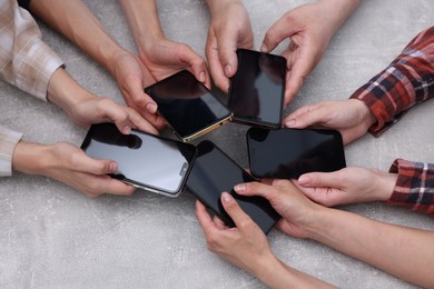 Photo of People holding smartphones with blank screens at grey textured table, closeup. Mockup for design