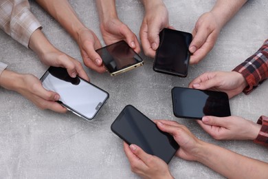 Photo of People holding smartphones with blank screens at grey textured table, closeup. Mockup for design