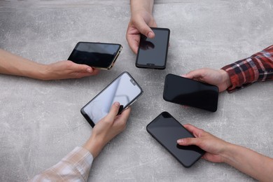 Photo of People holding smartphones with blank screens at grey textured table, top view. Mockup for design