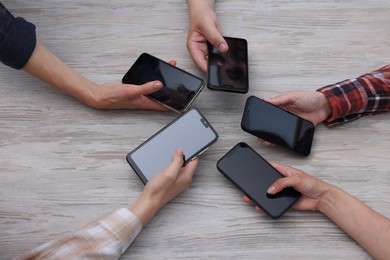 Photo of People holding smartphones with blank screens at wooden table, closeup. Mockup for design