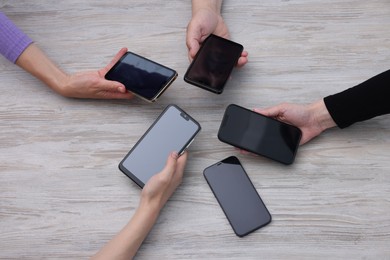 Photo of People holding smartphones with blank screens at wooden table, closeup. Mockup for design