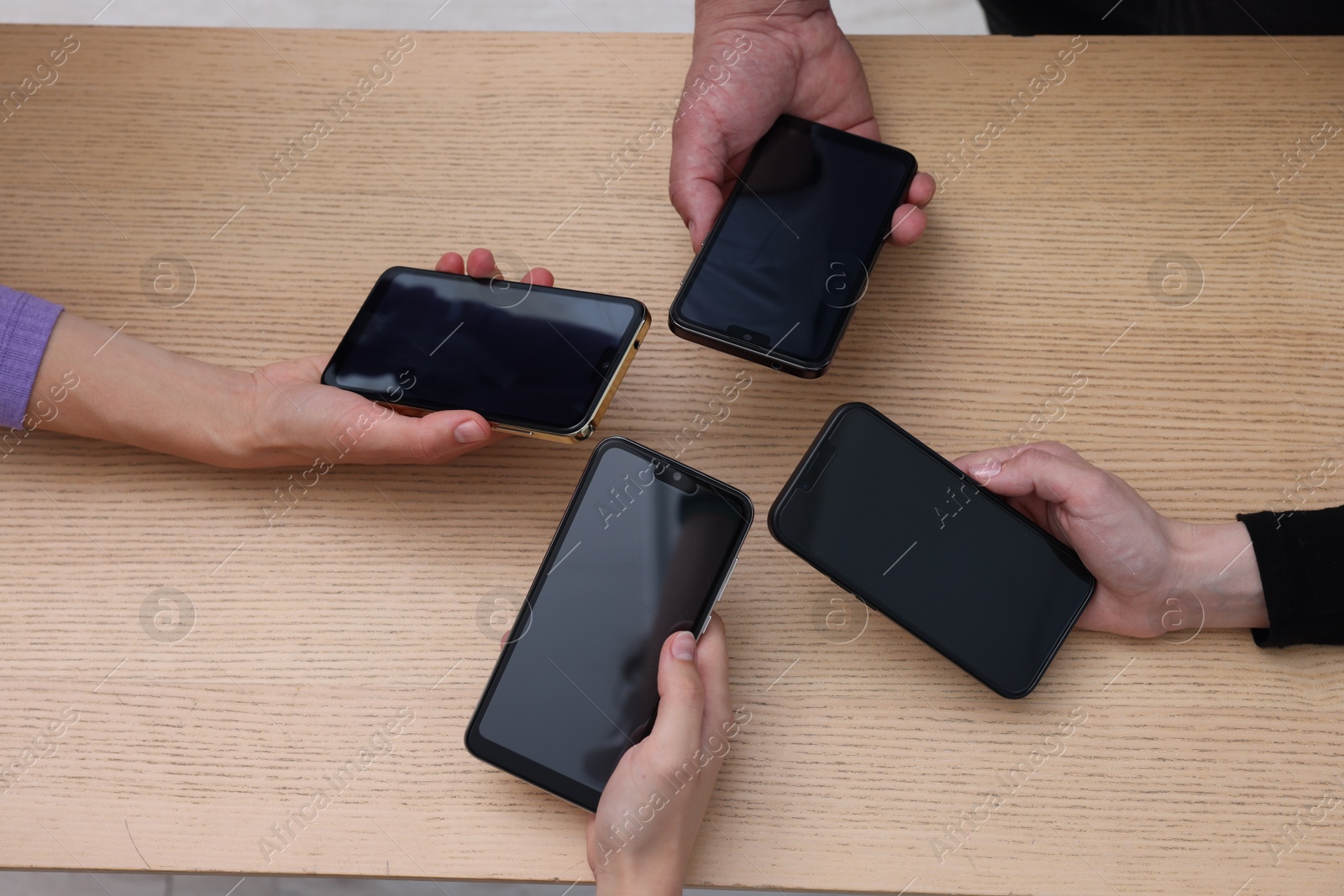 Photo of People holding smartphones with blank screens at wooden table, closeup. Mockup for design