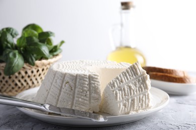 Photo of Tasty ricotta (cream cheese) and knife on grey textured table, closeup