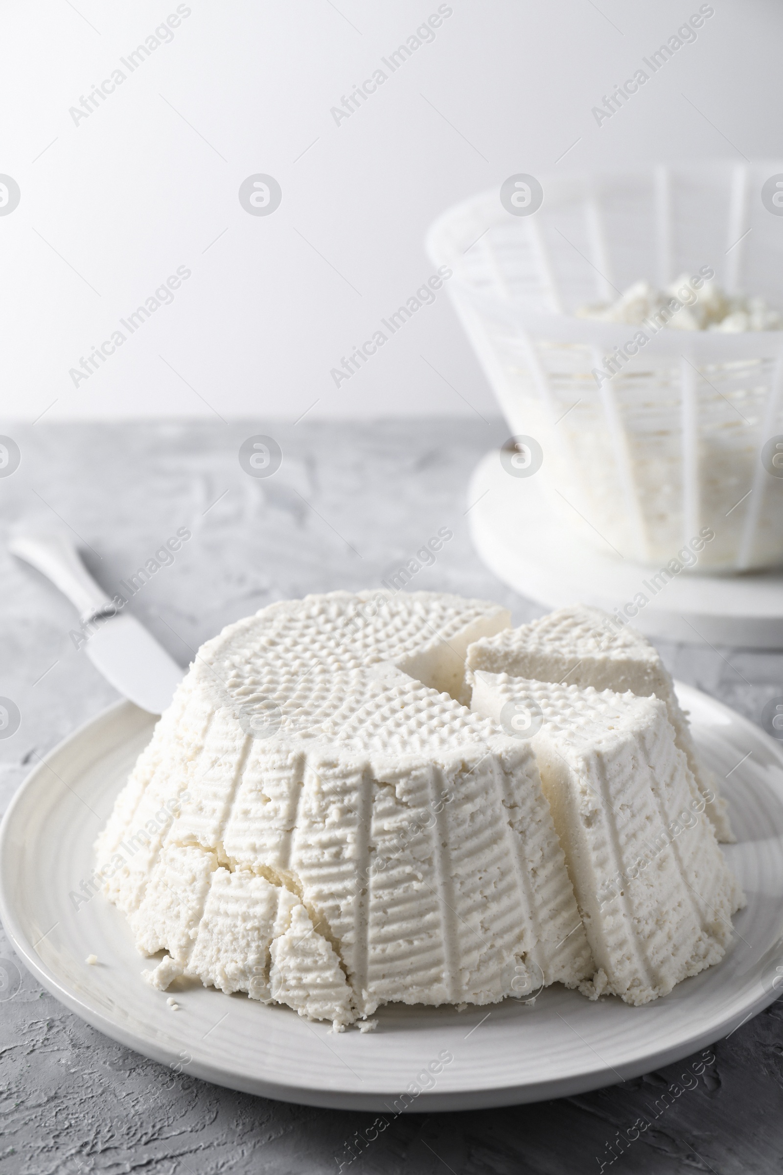 Photo of Tasty ricotta (cream cheese) and knife on grey textured table, closeup