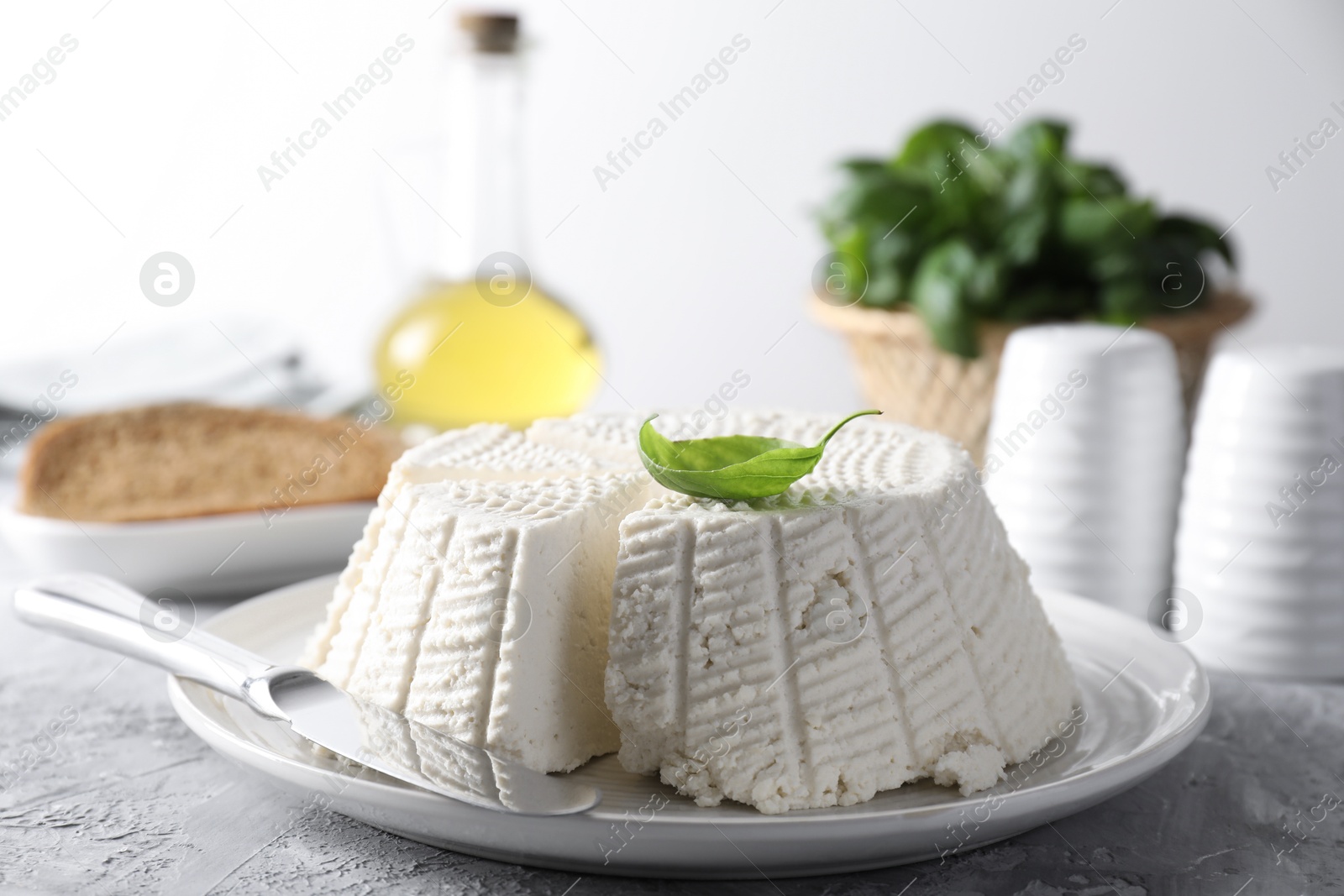 Photo of Tasty ricotta (cream cheese) and knife on grey textured table, closeup