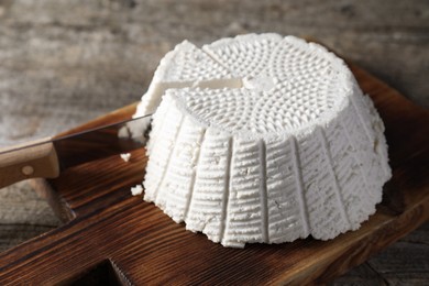 Photo of Tasty ricotta (cream cheese) and knife on wooden table, closeup