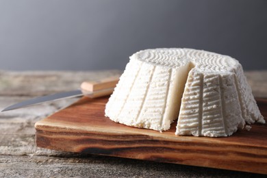 Photo of Tasty ricotta (cream cheese) and knife on wooden table, closeup