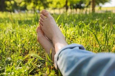 Photo of Woman sitting barefoot on green grass outdoors, closeup