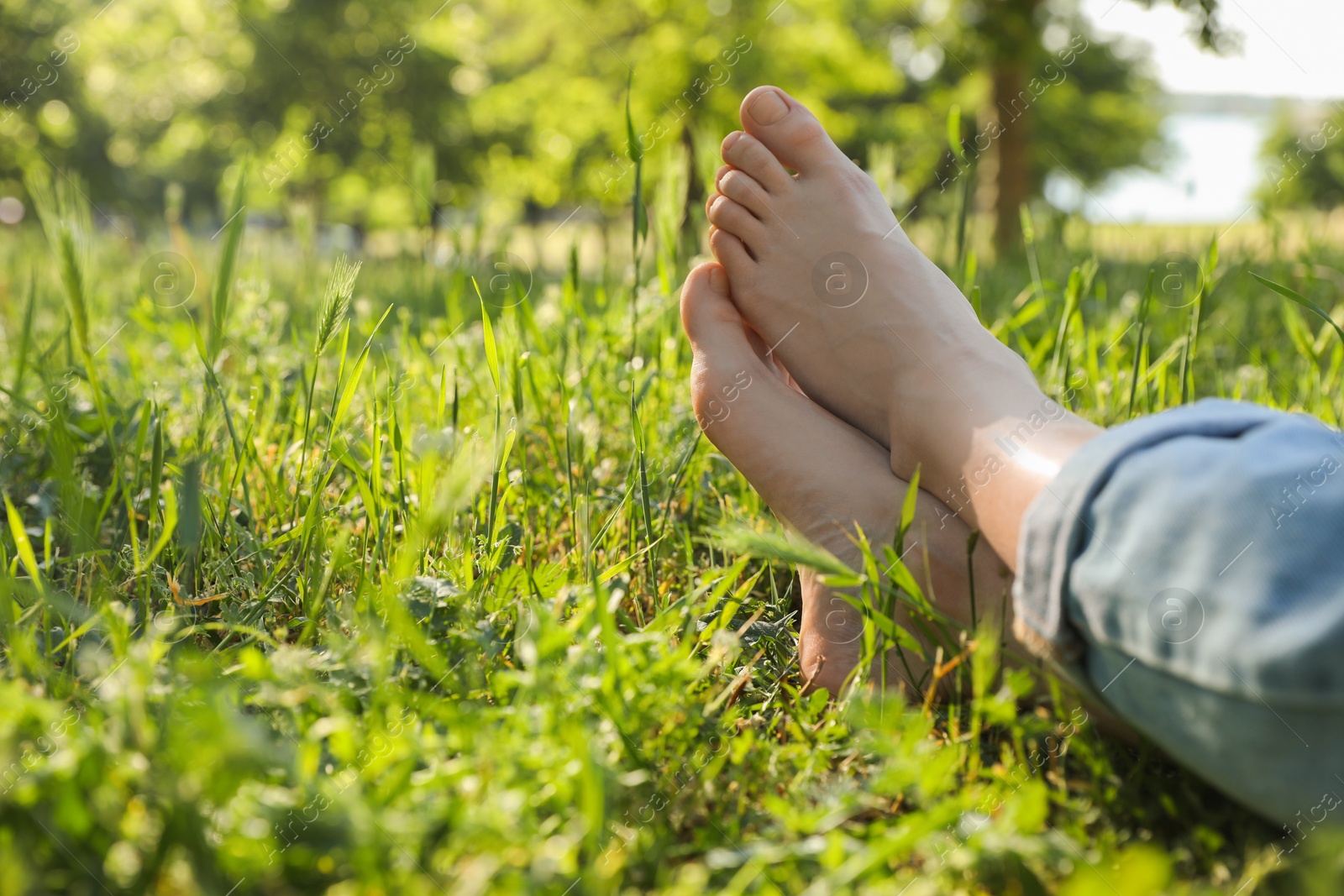 Photo of Woman sitting barefoot on green grass outdoors, closeup. Space for text