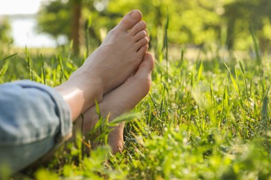 Woman sitting barefoot on green grass outdoors, closeup. Space for text