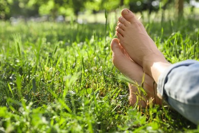 Photo of Woman sitting barefoot on green grass outdoors, closeup. Space for text