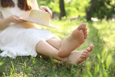 Photo of Woman sitting barefoot on green grass outdoors, closeup