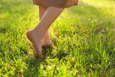 Photo of Woman walking barefoot on green grass outdoors, closeup