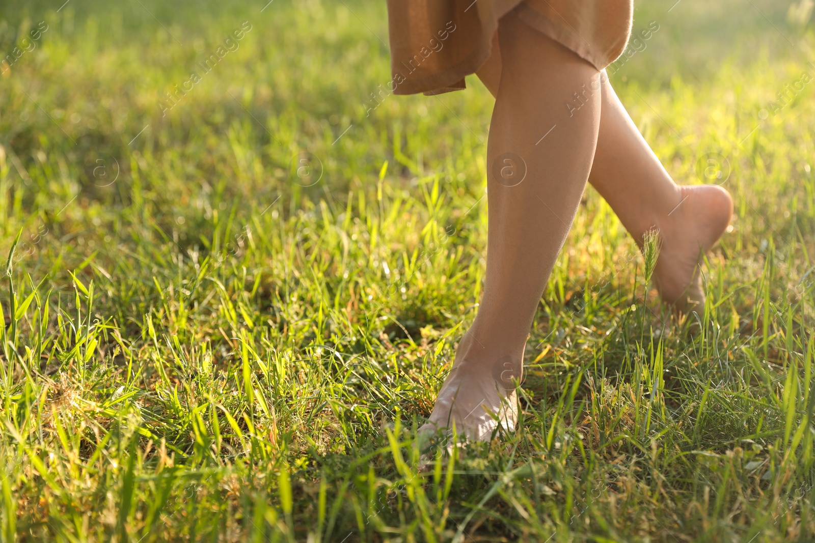 Photo of Woman walking barefoot on green grass outdoors, closeup. Space for text