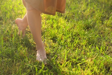 Photo of Woman walking barefoot on green grass outdoors, closeup. Space for text