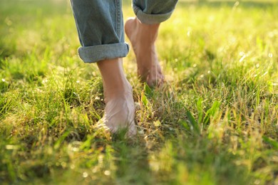 Photo of Woman walking barefoot on green grass outdoors, closeup