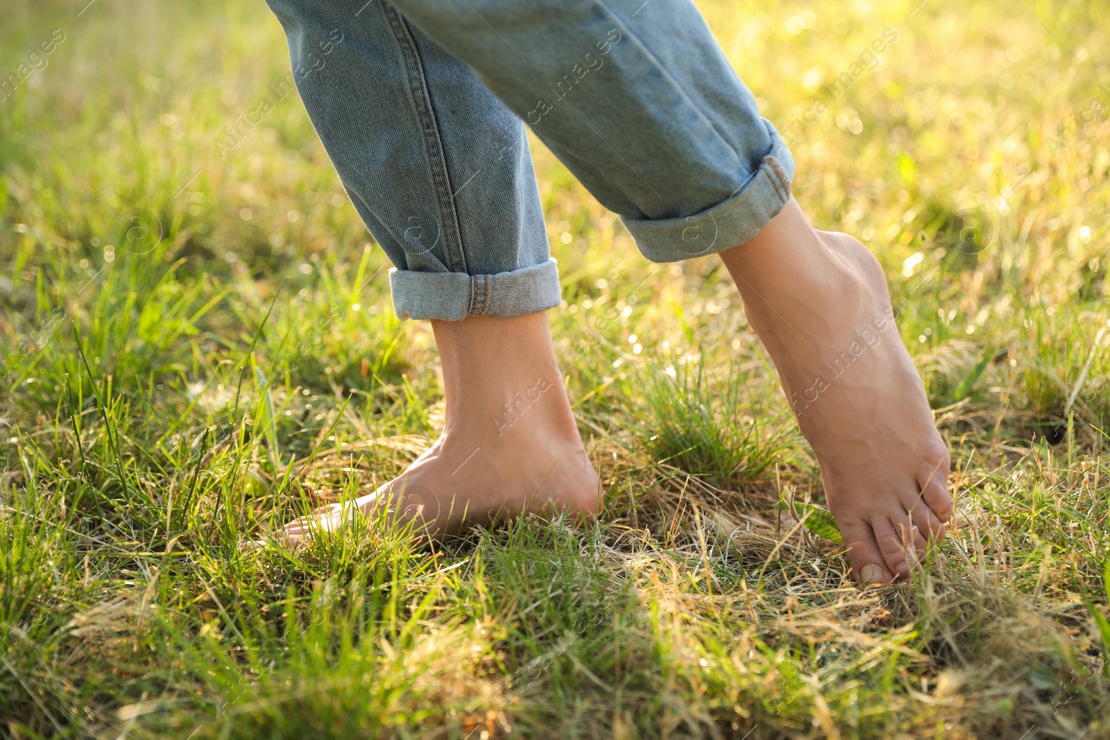 Photo of Woman walking barefoot on green grass outdoors, closeup